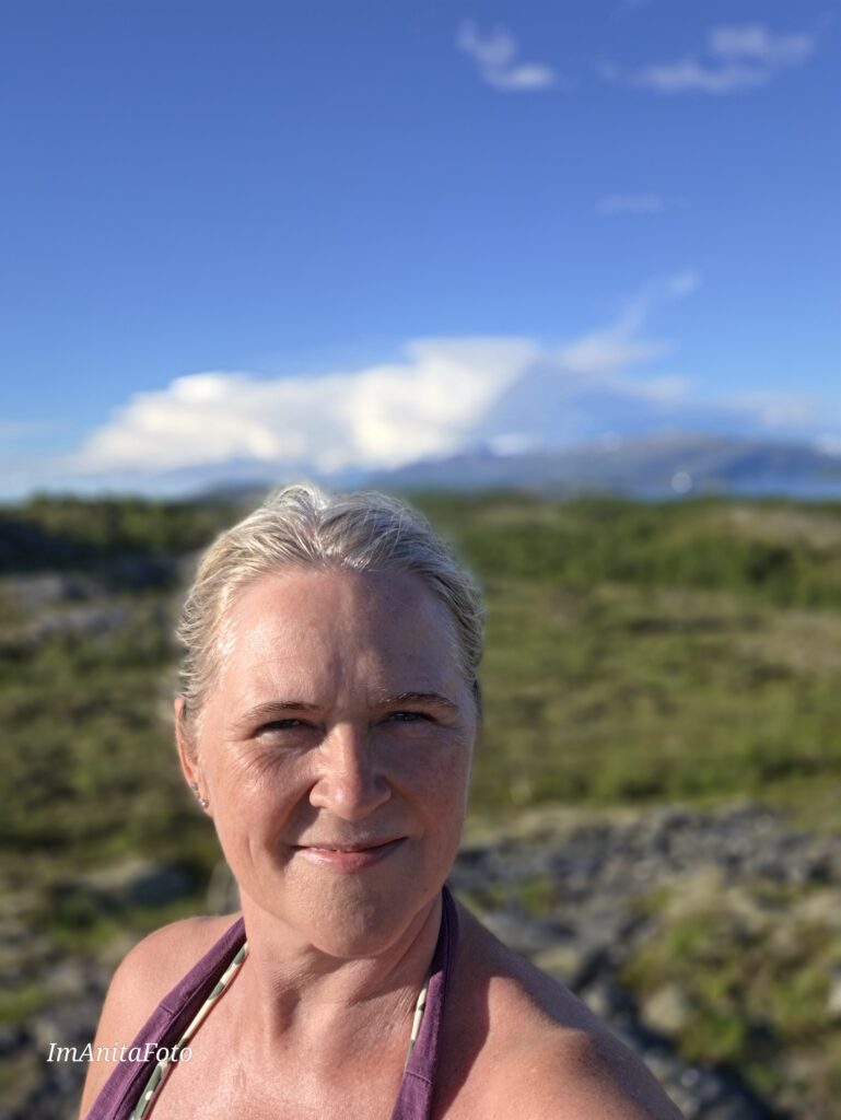 Anita Sofie Hauknes på myrlandskap på Helgeland med fjell og åpen himmel bak seg